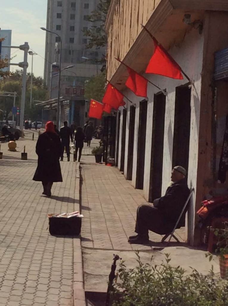 우루무치의 붉은 중국 국기 아래의 그늘에 있는 모습