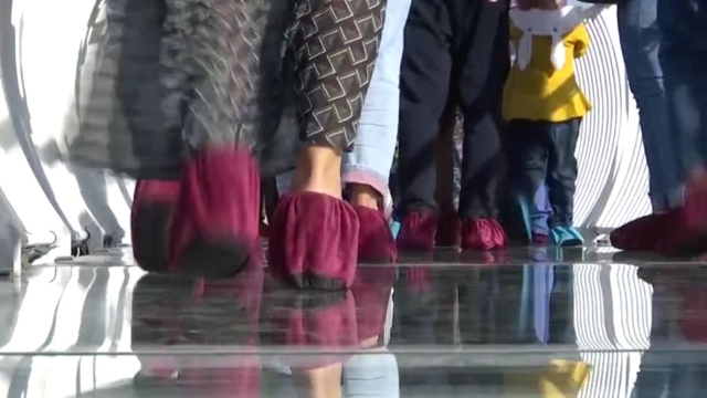 덧신을 신고 ‘산산이 부서지는’ 특수 효과 및 효과음이 있는 유리를 지나고 있는 관광객들